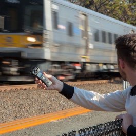 A creator using a Zoom H1N to capture audio from a nearby train passing by.